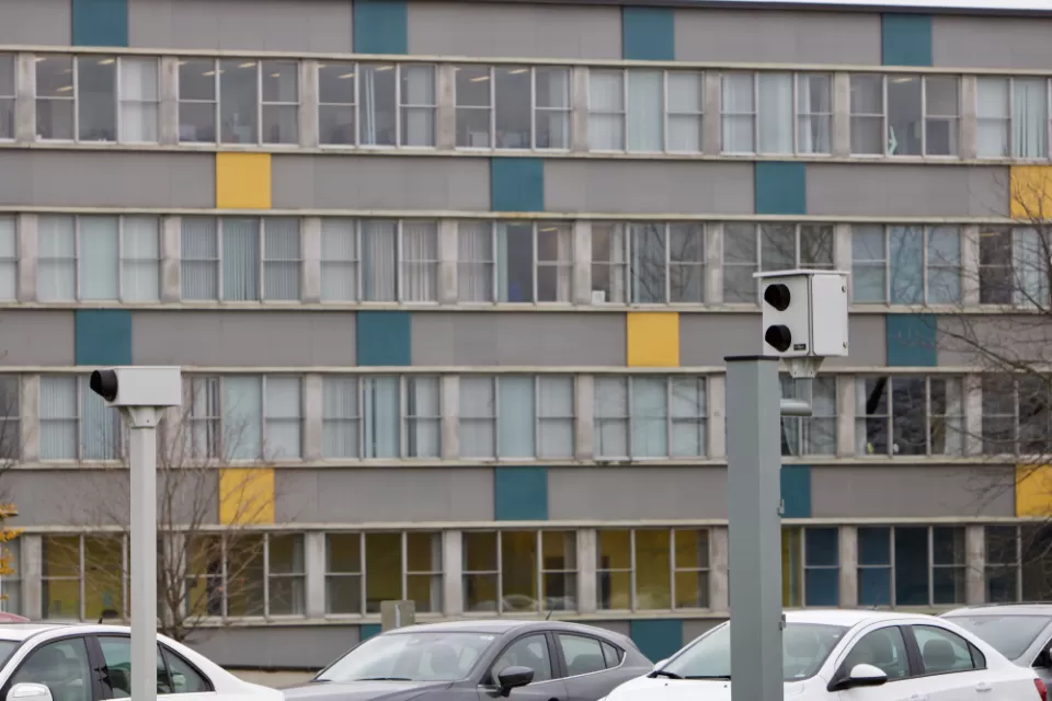 Two white traffic enforcement cameras above a road in Ottawa, Canada with a colorful multistory building in background